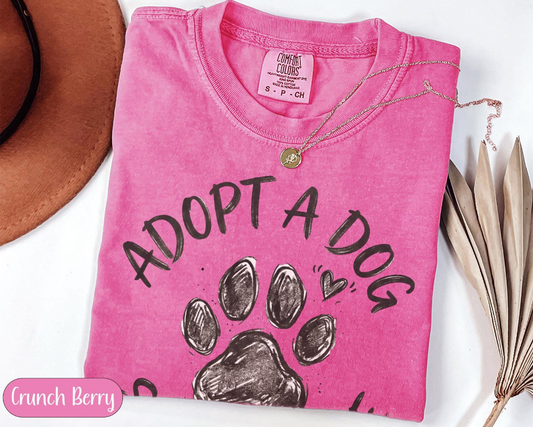 Pink t-shirt with 'Adopt a Dog' text and paw print design on a white background.