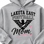 A close-up of a light heather gray hoodie featuring a graphic print that reads 'LAKOTA EAST FOOTBALL Mom' with a black eagle logo, lightning bolt, and pink hearts.