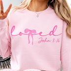A person wearing a light pink crewneck sweatshirt with the word 'loved' in pink script and 'John 3:16' in smaller text below, shown in a cropped social-style listing image with 'PNG SVG' and 'Buy with Apple Pay' overlays.